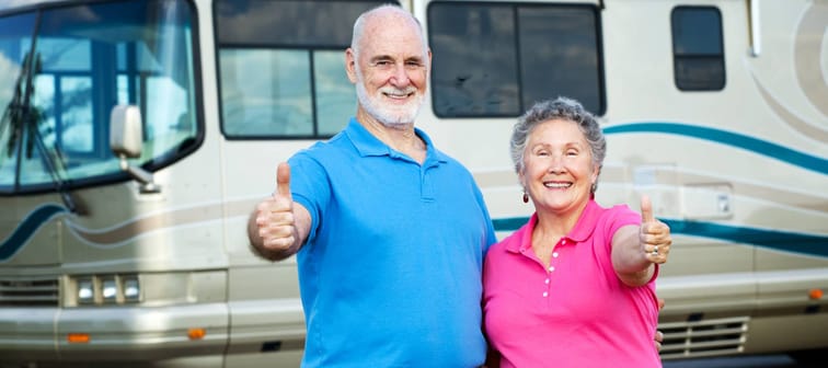 Older couple poses with their thumbs up in front of an RV.