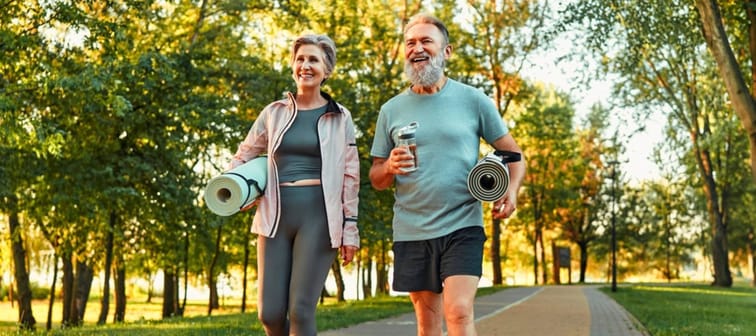 Sporty couple in their 60s, walking outside with yoga mats