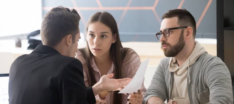 Young couple look distressed while speaking with a business person in an office.