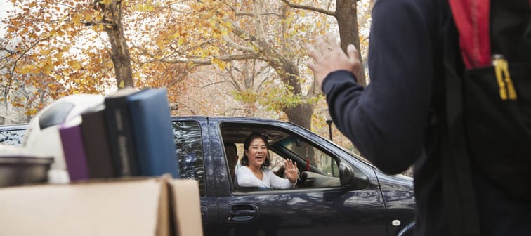 Mom waves goodbye to son from car as she drops him off for college.