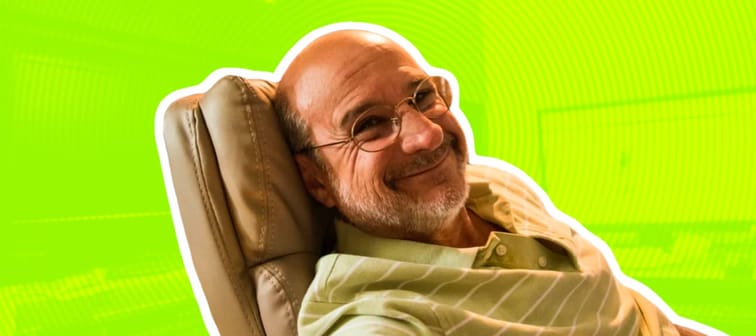 Smiling older man reclining in leather executive chair at his desk with his computer monitor in background