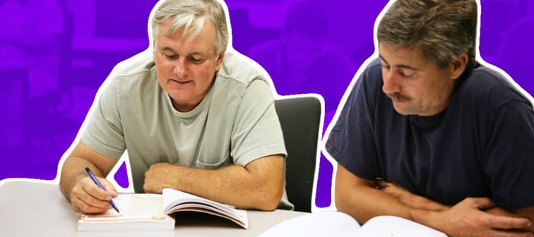 Two middle aged men sit at a desk, studying.