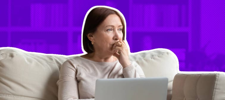 Older woman looks off into the distance, sitting on a couch with her laptop on her lap.