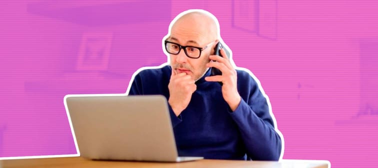 Wondered middle aged man making a call and using laptop while working from home.