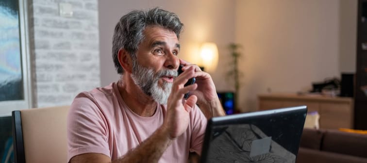 Older man working from home and using phone.
