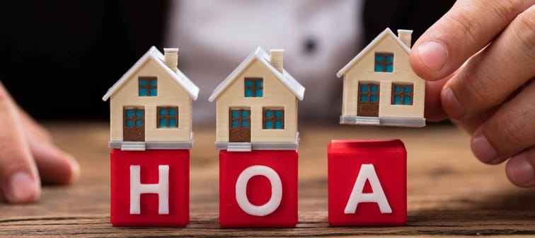 Businessperson's hand placing house model over red HOA blocks on wooden desk