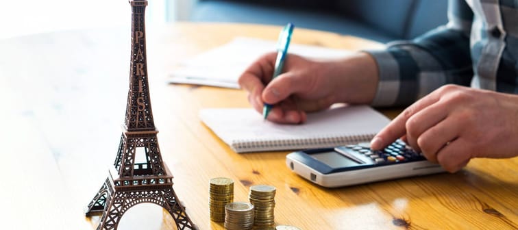 Man counting travel budget, vacation expenses or insurance cost. Traveler planning holiday in Europe. Cheap flights and hotel. Money and little Eiffel Tower souvenir from Paris on table.