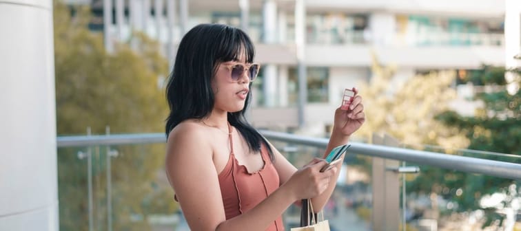 A young lady attempts to input the CVV number of a credit card on her cellphone during an impulsive online transaction while standing on a balcony.