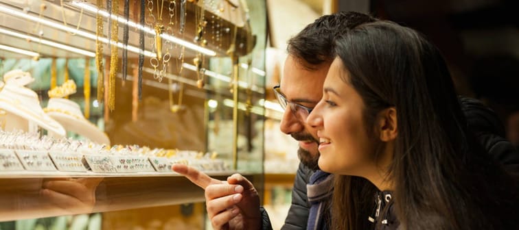 Happy beautiful young couple choosing a wedding rings while smiling and pointing into shop window.