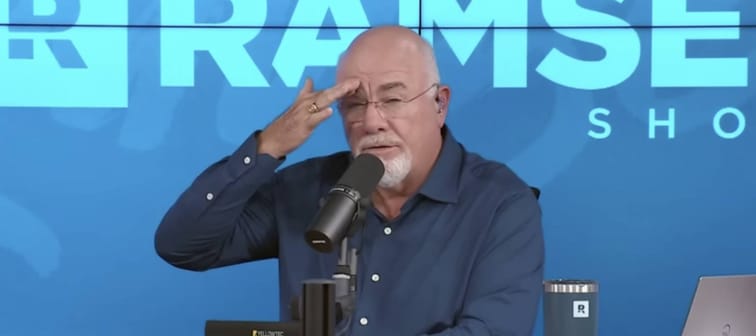 Dave Ramsey speaks on set of his show with his hand on his brow.