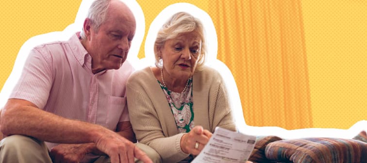 Older couple sit on a couch, looking seriously at papers.
