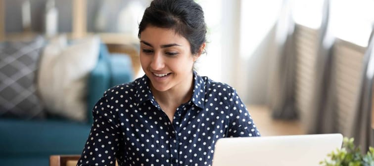 Happy millennial Indian girl sit at desk in living room