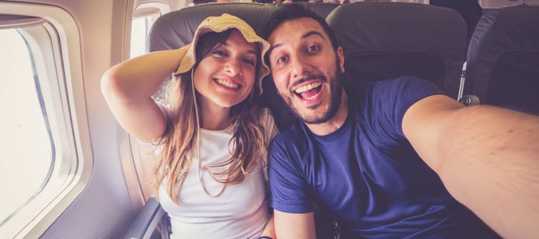 Smilling young couple pose for a selfie on an airplane.