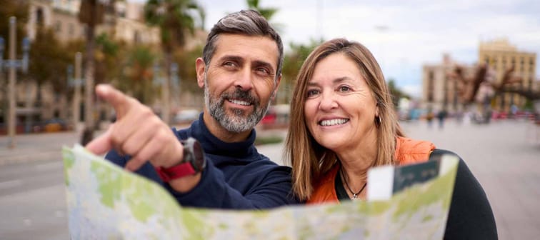 Middle-aged Caucasian couple with travel map in hands looking and pointing places of tourist interest.