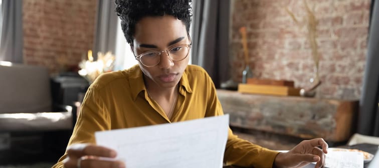 Focused young African American woman in eyeglasses looking through paper documents