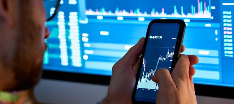 male investor analyst on mobile phone looking at cryptocurrency financial stock market graph