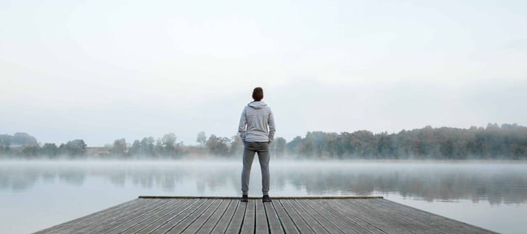Young man standing alone on wooden footbridge and staring at lake.