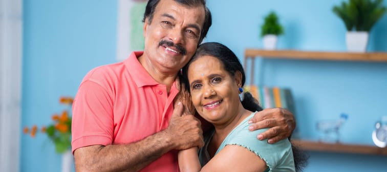 Older South Asian couple smiling while holding each other.