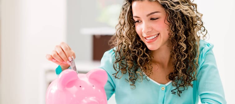 Young woman putting money into a piggy bank.