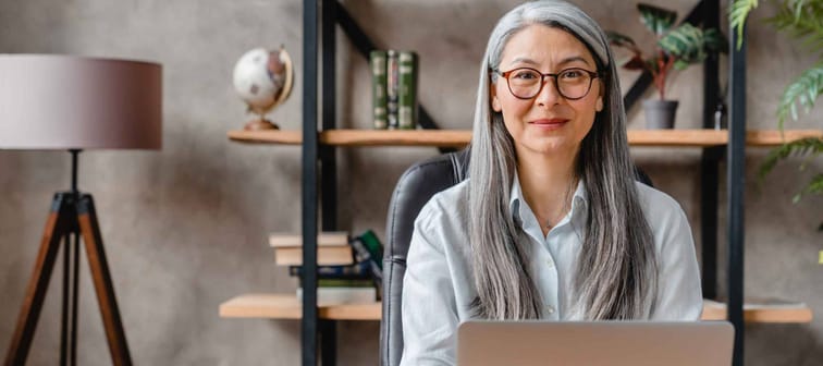 Confident middle-aged grey-haired woman working on the laptop in modern office
