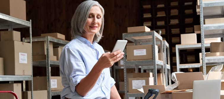 Female mature senior small business owner using mobile app checking parcel box.