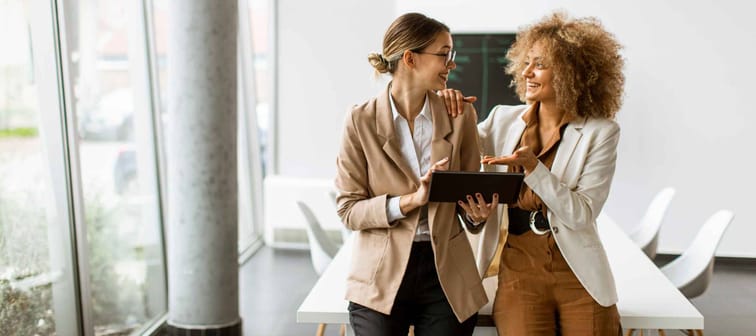 Two young women holding digital tablet and working in modern office