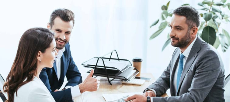 investors in suits giving dollar banknotes to advisor at office