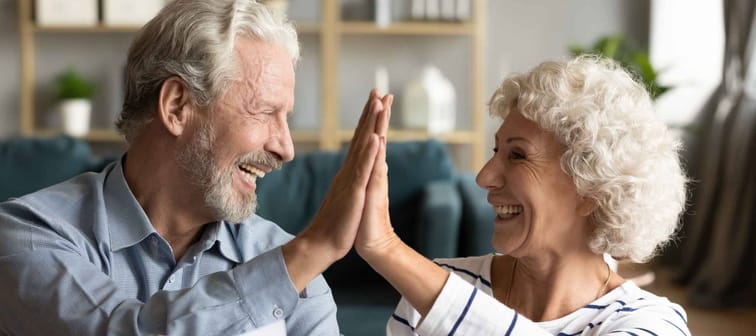 Smiling old hoary man giving high five to mature wife, finishing calculating domestic expenses, managing family savings or budget, happy retired couple feeling excited of having enough money.