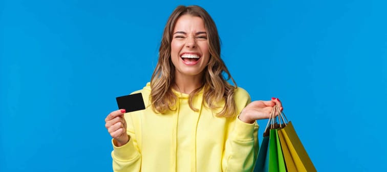Carefree emotive, smiling happy pretty blond girl using credit card to waste some money in mall, holding shopping bags, buy gifts or presents, treat yourself day, laughing joyfully
