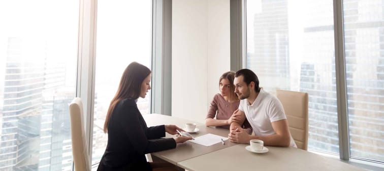 Young family couple meeting with bank worker to sign loan contract, discussing banking credit, personal insurance or mortgage investment, manager showing clients build project on tablet