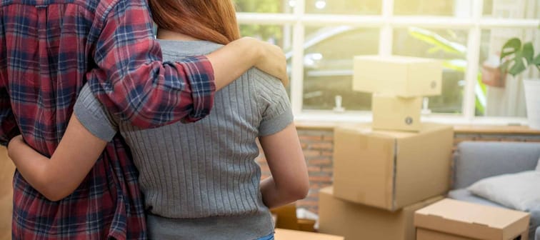 Back side of Asian young couple hugging together over the big cardboard box and sofa when moving in new house, Moving and House Hunting concept