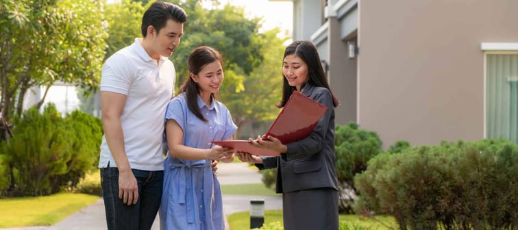 Asian woman Real estate broker agent showing a house detail in her file to the young Asian couple lover looking and interest to buy it. Buying a new house.