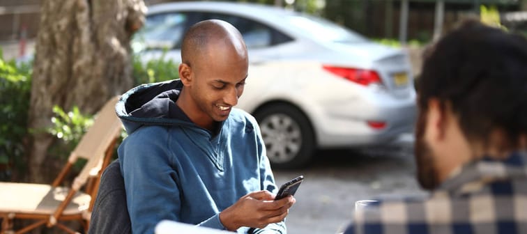 brown man in blue hoodie smiling at phone