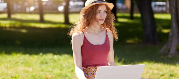 young student female smiling in park with laptop sitting on bench