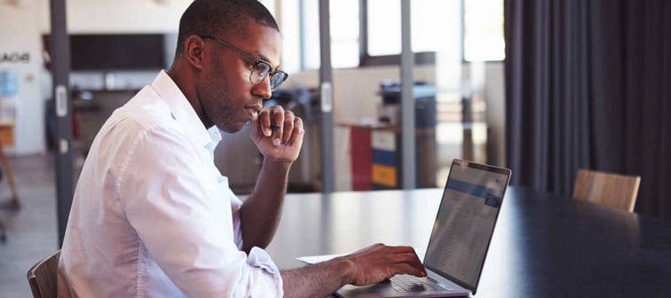Young black man in wearing glasses using laptop in office