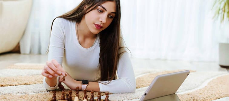 Teen girl plays chess alone. Home hobby, learn to play chess with tablet from Internet.