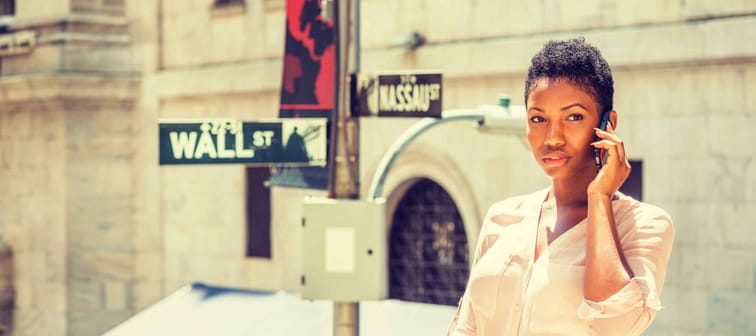 Young African American Businesswoman traveling, working in New York, standing on Wall Street by street signs under sun, talking on cell phone.