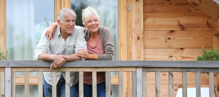 Senior couple standing oustide log cabin in countryside