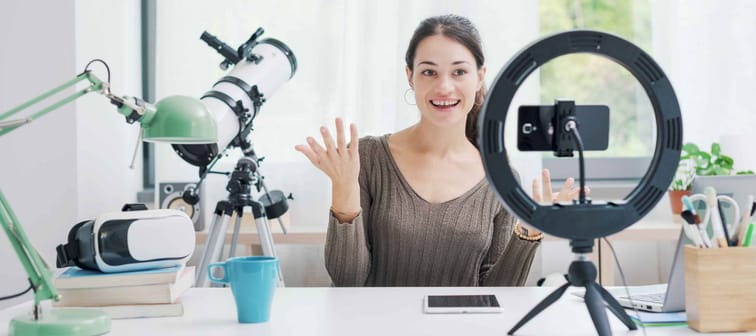 Young creative girl recording videos for social media at home, she is using a smartphone and a ring light