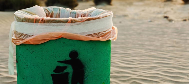 Green waste container on sandy beach. Plastic waste pollution and greenwashing.
