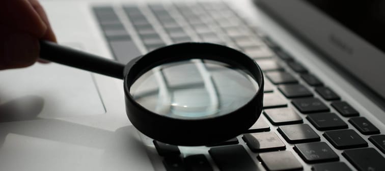 person holding magnifying glass over laptop keyboard