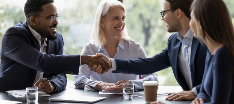 Smiling diverse businesspeople shake hands get acquainted greeting at team meeting in office.