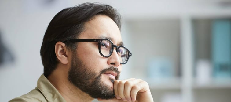 Close-up of serious creative young Asian man with beard being deep in thoughts while working on project in office