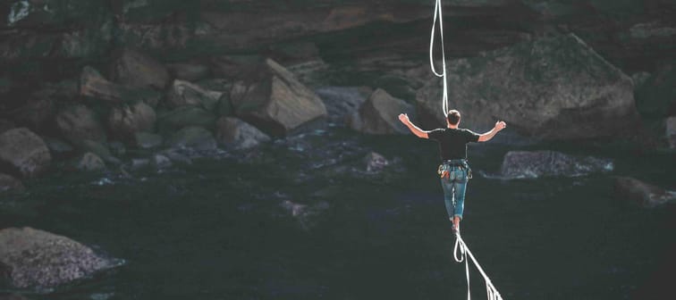 person on a tightrope or slack line perfectly balancing between two cliffs taking a risk for a reward