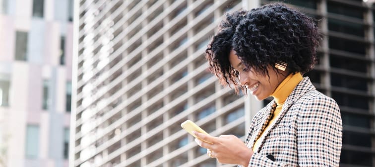 Close-up of african american businesswoman checking her mobile phone while walking to work at financial city district. Business concept.