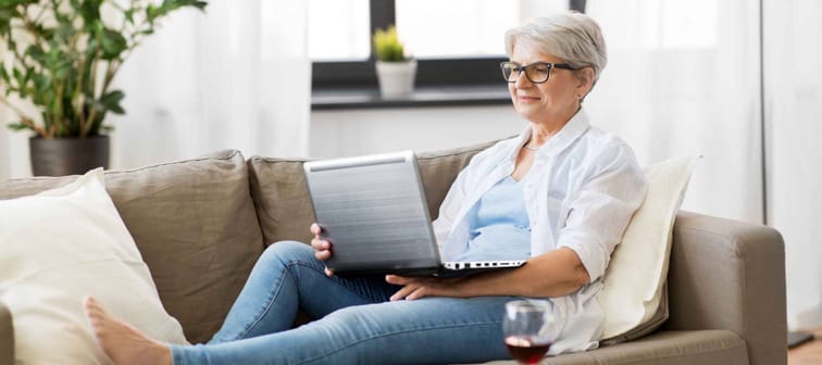 technology, old age and people concept - happy senior woman in glasses with laptop computer and glass of wine at home