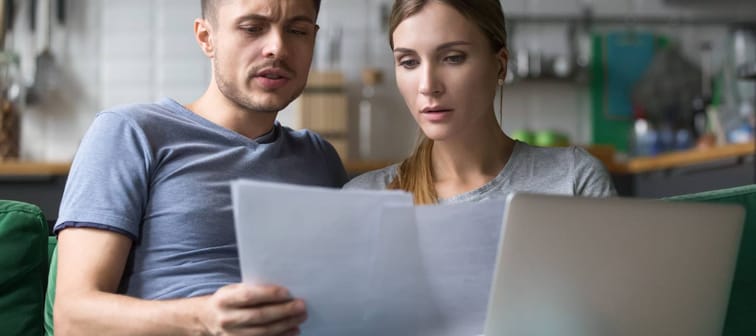 Serious confused couple checking high domestic bills with papers and laptop