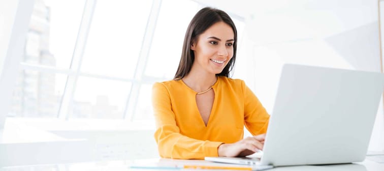 Business woman in orange shirt using laptop computer and sitting by the table in office