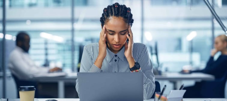 Young Black Woman Office Worker Uses Laptop, Headache, Migraine. Overworked Accountant Feeling Project Pressure, Massages Her Head, Temples. Front View Portrait