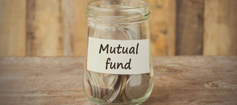 Coins in glass money jar with mutual fund label, financial concept. Vintage wooden background